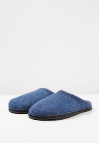 Blauwe vilten slippers met een afgeronde neus, zachte textuur en een zwarte rubberen zool. Open achterkant ontwerp, met een gestikte rand rondom.