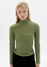 Langärmliges, olivgrünes Ripp-Turtleneck-Oberteil, enganliegendes Design, weiche Textur, kombiniert mit einem schwarzen Unterteil. Minimalistischer Stil, keine Muster.