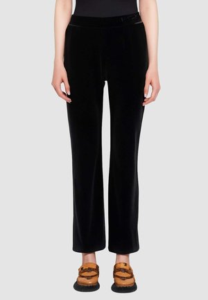 Pantaloni in velluto nero con design a gamba dritta, caratterizzati da una texture liscia e una cintura elastica. Abbinati a scarpe slip-on marroni.