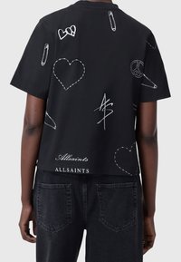 Mustat puuvillaiset lyhythihaiset T-paidat, joissa on valkoisilla ommelluilla kuvioilla, kuten sydämillä ja turvatipoilla, ja "Allsaints" -brändi helman kohdalla.