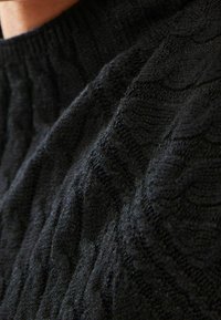 Pull noir en maille tricotée avec un motif de câble texturé, col rond et poignets côtelés. Le matériau semble doux et chaud.