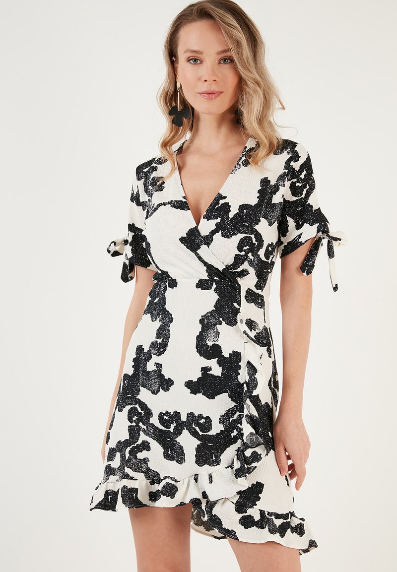Black and white floral print wrap dress with short sleeves, side ruffle detailing, and tie accents. Made from textured fabric.