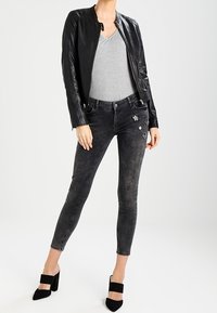 Schwarze Lederjacke über einem grauen V-Ausschnitt-Oberteil, kombiniert mit schwarzen Skinny-Jeans mit silbernen Sternelementen und schwarzen High-Heels.