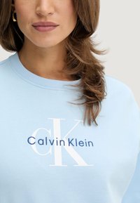 Felpa azzurro chiaro con logo "Calvin Klein" ricamato in bianco e blu navy, con scollo classico a girocollo e polsini a costine.
