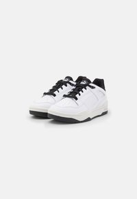 Bílé tenisky s černými akcenty, vyrobené z syntetické kůže. Mají texturovanou špičku, černé šňůrky a polstrovaný límec.