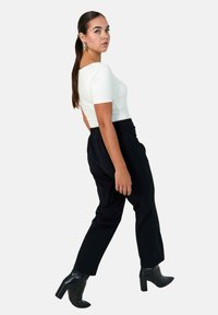 White fitted top with short sleeves paired with loose black trousers and black heeled boots. Model in profile against a plain background.
