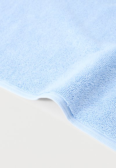 Ανοιχτό μπλε απαλό πετσετοειδές ύφασμα διπλωμένο ελαφρώς σε λευκή επιφάνεια, εμφανίζοντας την υφή με βρόχους του υφάσματος.