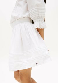 Jupe en coton blanc avec un design froncé, des rayures horizontales texturées, des accents en dentelle et un petit logo de la marque au bas.
