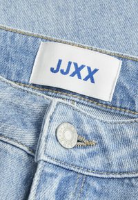 Svijetloplave traperice imaju ušivenu etiketicu s natpisom "JJXX" u plavoj boji. Srebrni gumb zatvara struk. Tekstura tkanine s suptilnim uzorcima.