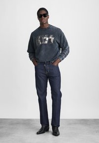 Mørkeblå denimjeans parret med en falmet sort sweatshirt, der har et sølvfarvet "KISS" grafisk motiv og nitter. Båret med sorte solbriller og støvler.
