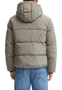Puffjacke in Hellgrau mit gestepptem Design, Kapuze und elastischen Bündchen. Kombiniert mit blauen Jeans in lässigem Schnitt.
