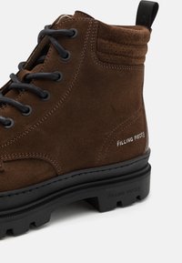 Bottine à lacets en daim marron avec semelle noire, col matelassé et marquage "Filling Pieces" sur le côté et la semelle.