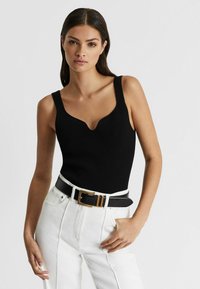 Schwarzes, geripptes Tanktop mit tiefem V-Ausschnitt, kombiniert mit hochtaillierten weißen Jeans und einem schwarzen Gürtel mit goldenen Akzenten.