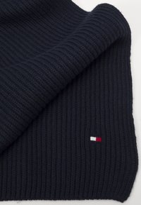 Marineblaue gestrickte Schal mit gerippter Textur. Besitzt ein kleines Logo-Patch in Rot, Weiß und Blau am unteren Rand. Weicher, dicker Stoff.