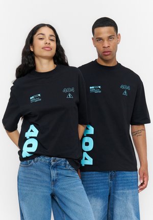 To personer iført sorte t-shirts med "404" grafik samt blå jeans står mod en ensfarvet hvid baggrund.