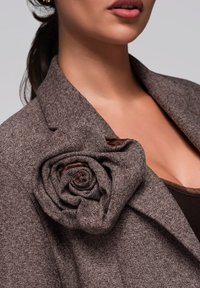 Blazer a spina di pesce marrone con un grande accento floreale in tessuto, caratterizzato da una finitura in satin in tonalità terrose, cuciture di precisione e rever affilati.