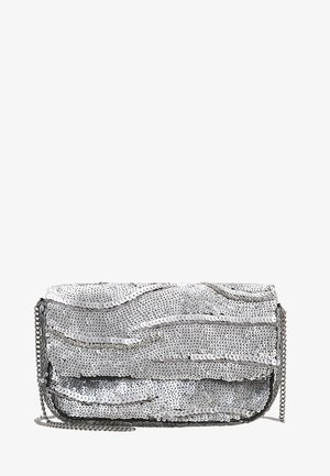 Bolso de mano de noche con lentejuelas plateadas con un patrón ondulado y una cadena delgada plateada sobre un fondo blanco.