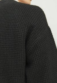 Schwarzer, strukturierter Pullover mit Karomuster. Übergröße mit Raglanärmeln und einem weichen, warmen Stoff. Sichtbare Nahtdetails.