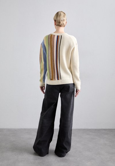 Cream sweater with multicolored vertical stripes on the back, paired with loose black pants. Sweater features ribbed cuffs and hem.