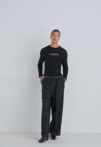 Camisa negra de manga larga con diseño gráfico gris en el pecho, combinada con pantalones negros holgados, creando una silueta relajada.