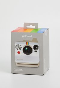 L'emballage de l'appareil photo instantané Polaroid Now présente une boîte blanche avec un objectif, des boutons et un dessus rayé coloré, étiqueté "Polaroid Now."