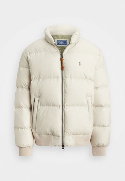 Casaco puffer em bege claro com fecho zip, punhos canelados e bolsos laterais. Apresenta um pequeno logótipo no peito e um acabamento texturizado.