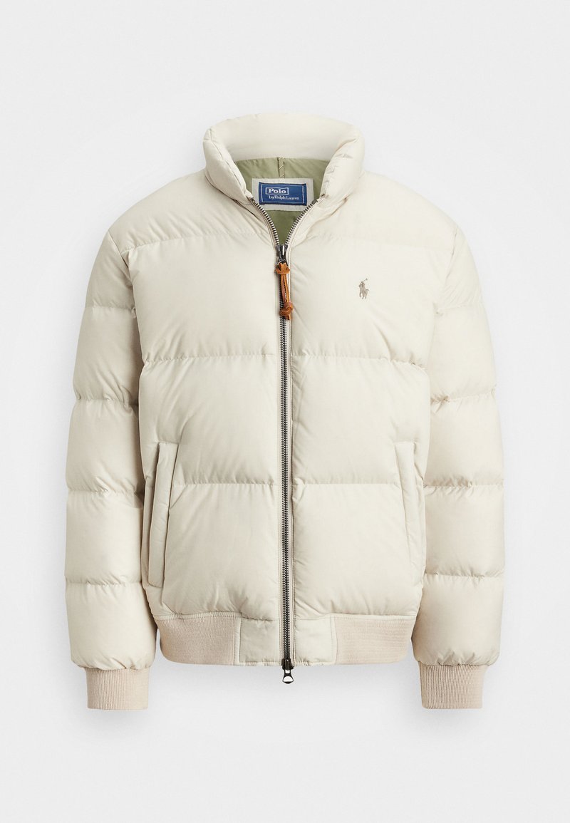 Pufferjack in licht beige met een ritssluiting aan de voorkant, ribgebreide manchetten en zijzakken. Beschikt over een klein logo op de borst en een gestructureerde afwerking.