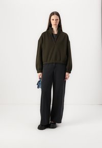 Dark green zip-up sweatshirt with a high collar, elastic hem, and balloon sleeves, paired with wide-leg black jeans and black shoes.