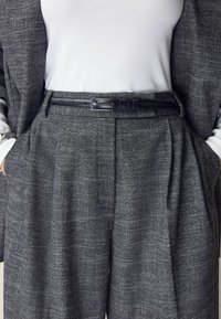 Grå texturerade kostymbyxor med fält, ett svart läderbälte och en vit ribbad långärmad skjorta under en matchande blazer.