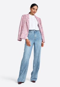 Blazer in tweed rosa sopra una blusa bianca a trama, abbinato a jeans a gamba larga in denim azzurro chiaro a vita alta. Tessuto liscio e vestibilità sartoriale.