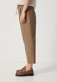 Pantalon en simili cuir marron à coupe fuselée, taille avec cordon de serrage et poches latérales, associé à des mocassins marron à semelle plate.