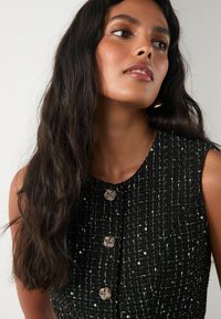 Czarna sukienka z tweedu o fakturowanej tkaninie, z srebrnymi akcentami, okrągłym dekoltem i trzema ozdobnymi, spiralnymi guzikami na przodzie.