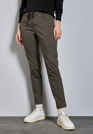 Pantalons en coton vert olive avec une taille élastique à cordon, coupe fuselée, poches avant et coutures latérales. Portés avec des baskets blanches et des chaussettes légères.