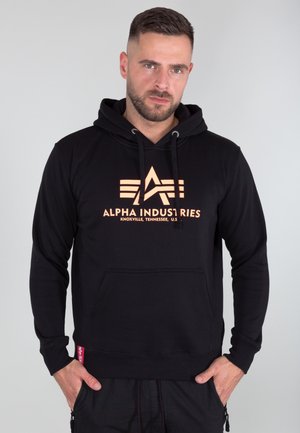 Black hoodie made of soft fabric, featuring an orange graphic logo, kangaroo pocket, drawstring hood, and ribbed cuffs and hem.