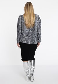Langarmshirt in einem grauen Schlangenprint, kombiniert mit einem schwarzen, figurbetonten Rock und metallisch- silbernen, kniehohen Stiefeln mit quadratischen Absätzen.