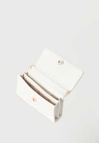 Λευκό καπιτονέ πορτοφόλι με χρυσό κουμπί κλεισίματος, ανοιχτό για να δείξει πολλαπλές θήκες και εσωτερική επένδυση μπεζ με εκτύπωση λογότυπου.