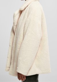 Cappotto plush oversize rosa chiaro con una texture pelosa, ampio colletto e maniche lunghe, che offre una vestibilità comoda e un aspetto morbido.