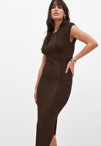 Abito a coste marrone con silhouette aderente, maniche corte e spacco laterale, caratterizzato da un design testurizzato per un tocco di interesse in più.