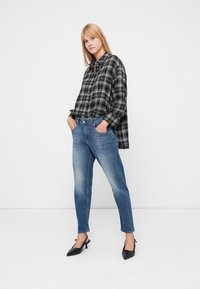 Camisa de cuadros en blanco y negro con botones, de ajuste holgado, combinada con jeans ajustados de color azul claro y zapatos de tacón alto negros con tiras en el tobillo.