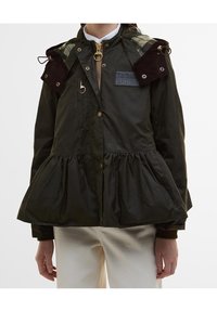 Donkergroene, lichtgewicht jas met een peplumzoom, corduroy accenten op de schouders, een gouden ritssluiting en een geborduurd merklabel op de borst.