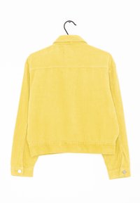 Gul manchesterjacka som hänger på en svart galge, sedd bakifrån, med långa ärmar och knäppta manschetter.