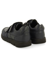 Vue arrière de chaussures en cuir bleu foncé avec une sangle en Velcro, présentant une texture douce et une semelle en caoutchouc noir durable.