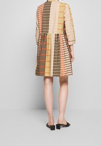 Kurzes Kleid aus gemustertem Stoff mit einem Mix aus beige, braun und orange karierten Designs, mit einem ausgestellten Rock und rundem Kragen.