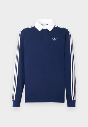 Mornarsko modra polo majica z dolgimi rokavi, bombažno blago, bel ovratnik, z značilnimi tremi belimi črtami vzdolž rokavov in majhnim logotipom na prsih.