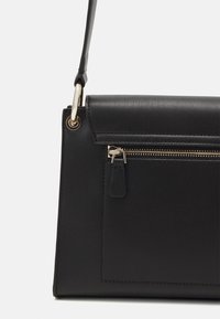 Borsa a mano in pelle nera con design strutturato, dotata di tasca con zip, dettagli in metallo e tracolla removibile. Texture liscia e linee pulite.