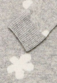 Ljusgrå tröja med en mjuk textur, ribbade ärmslut och ett vitt blommönster. Tyget verkar varmt och mysigt.