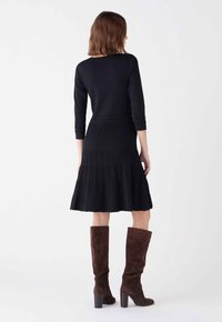 Robe plissée noire avec un corsage ajusté et des manches 3/4. Portée avec des bottes en suède marron jusqu'au genou et un détail de ceinture texturé.