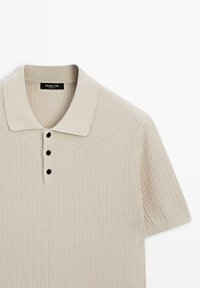 Polo beige côtelé à manches courtes avec un col doux et trois boutons noirs sur la patte de boutonnage avant.
