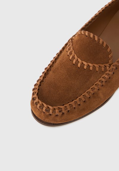 Καφέ μοκασίνι από σουέτ με στρογγυλεμένη μύτη, πλεχτές δερμάτινες διακοσμήσεις και αντίθετη ραφή κατά μήκος της άκρης. Λεία εσωτερική επένδυση.