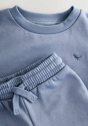 Világoskék pulóver bordázott nyakkivágással és kis dinoszaurusz logóval. A hozzá illő melegítőnadrág rugalmas derékbőséggel és húzózsinórral rendelkezik.